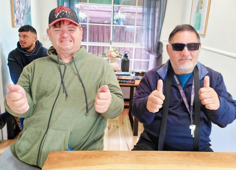 Two disabled friends smiling at the camera with thumbs up